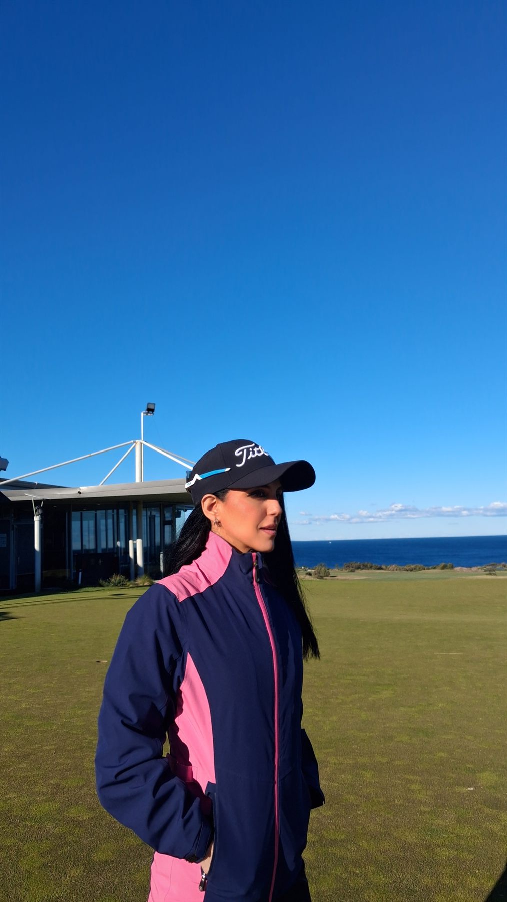 Rukmini Mehta in a Titleist cap beside the coastal clubhouse at St Michael's Golf Club