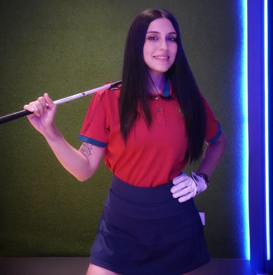 Rukmini Mehta smiling in an indoor golf studio with a club across her shoulders