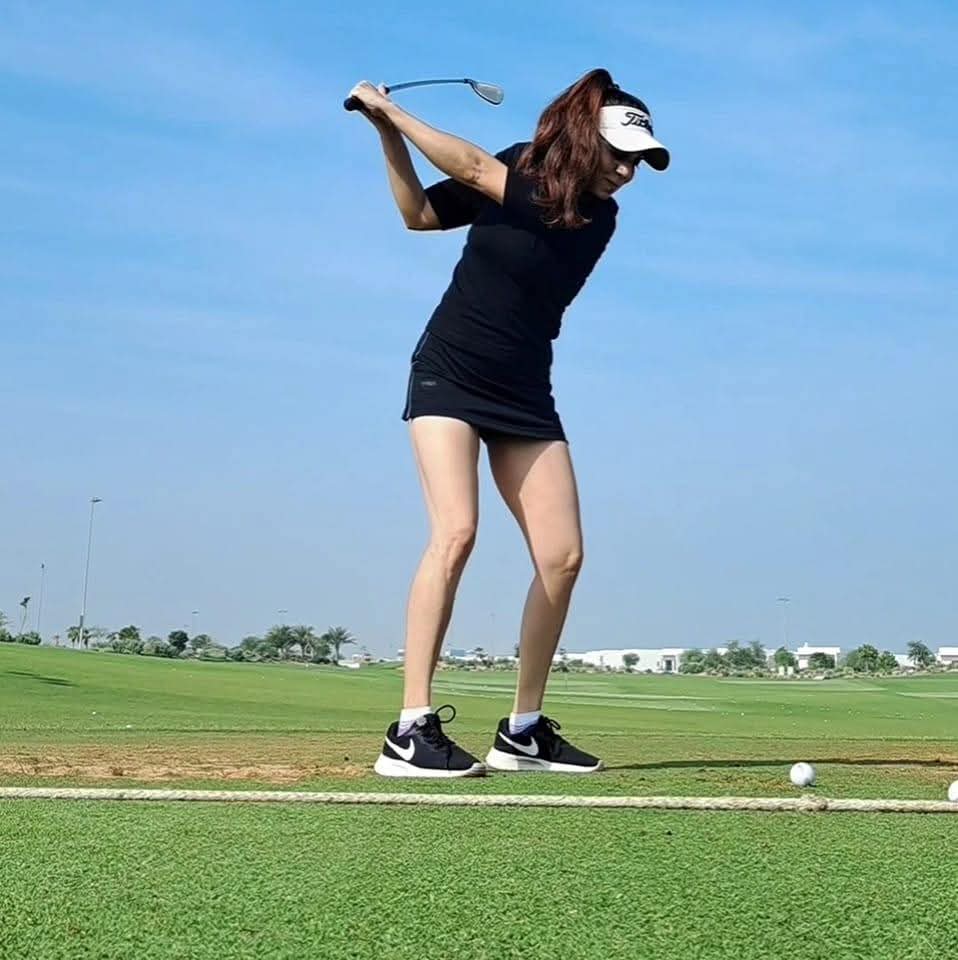 Rukmini Mehta at the top of her backswing on a driving range under a clear blue sky