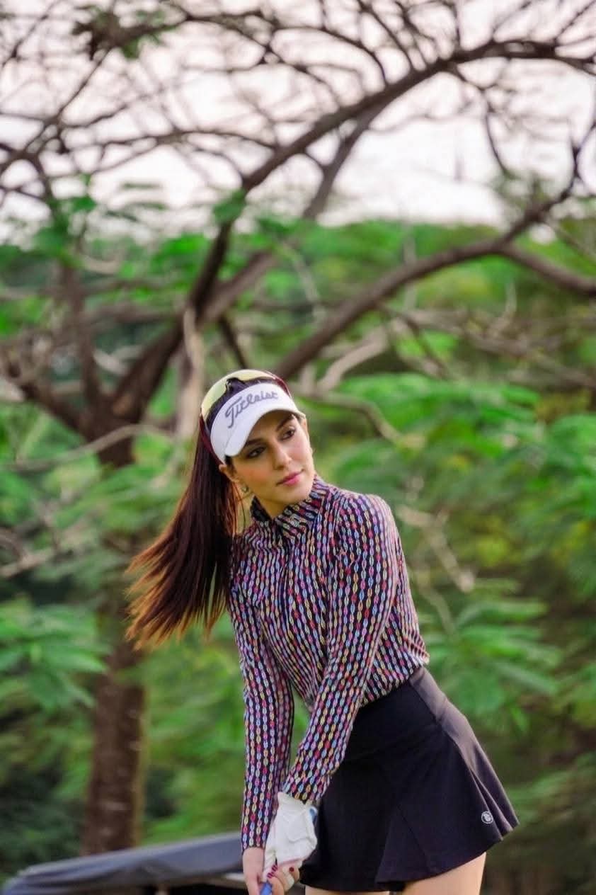 Portrait of Rukmini Mehta in a patterned top and Titleist visor with blurred greenery behind