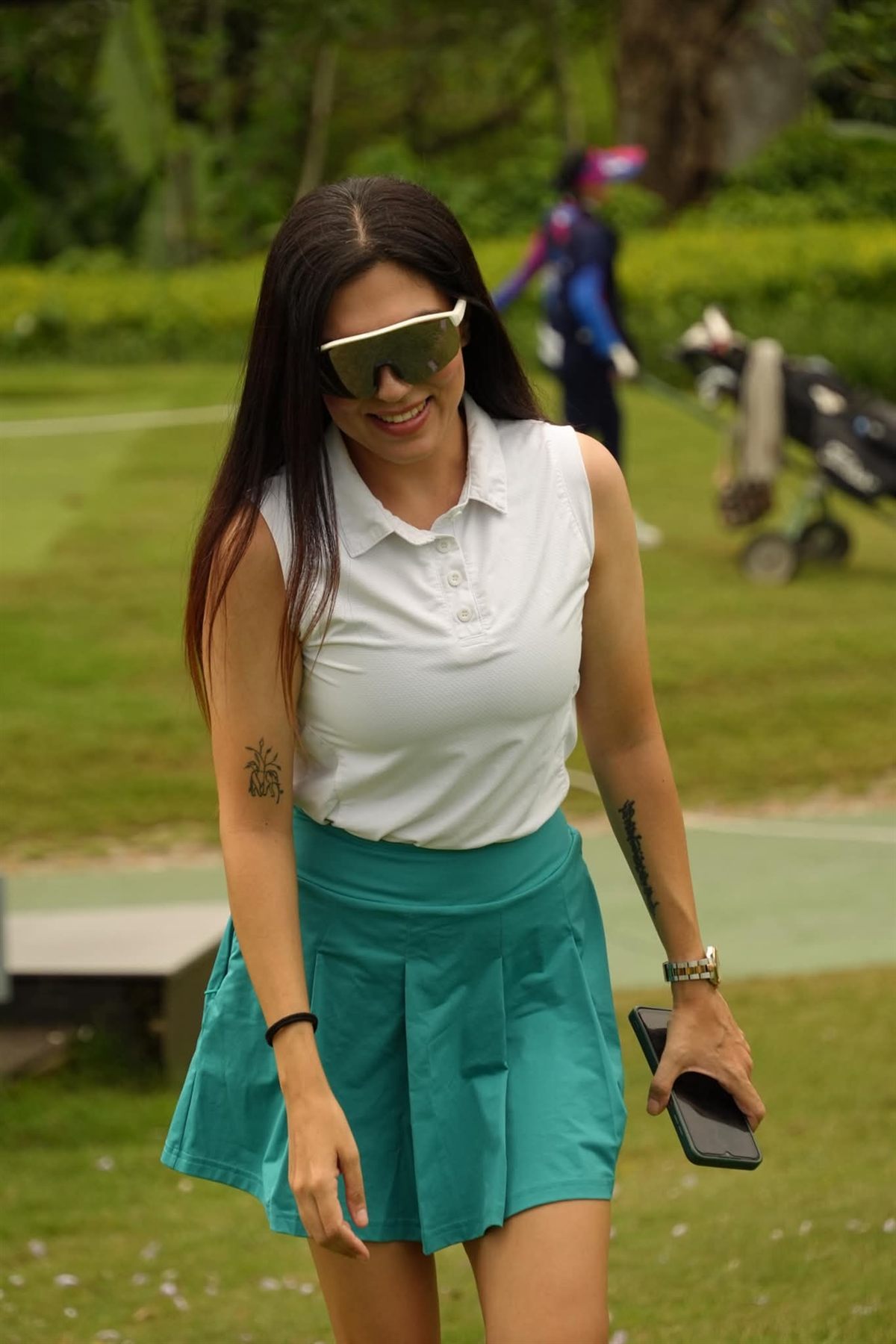 Rukmini Mehta smiling while walking on a golf course in a white polo and teal skirt